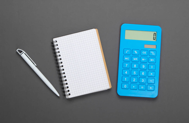 Calculator met een notitieboekje op een grijze achtergrond. gezinsbudgetbeheer. Bovenaanzicht - Foto, afbeelding