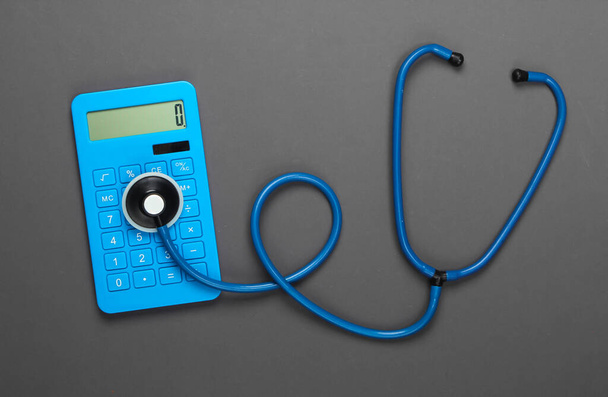 Gesundheitskonzept. Taschenrechner mit Stethoskop auf grauem Hintergrund. Ansicht von oben - Foto, Bild