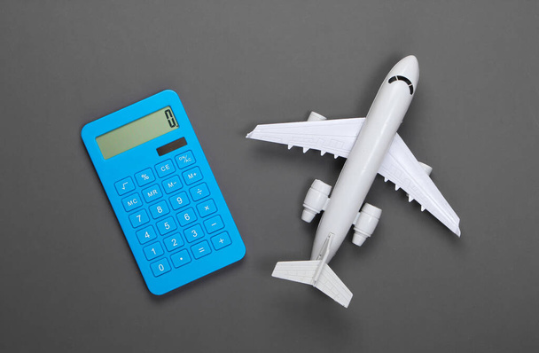 Rekenmachine en beeldje van een passagiersvliegtuig op een grijze achtergrond. Berekening van de kosten van vliegreizen. Bovenaanzicht - Foto, afbeelding