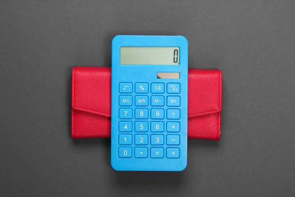 Beheer gezinsbudget. Winkelkosten. Blauwe rekenmachine met rode leren portemonnee op grijze achtergrond. Bovenaanzicht - Foto, afbeelding