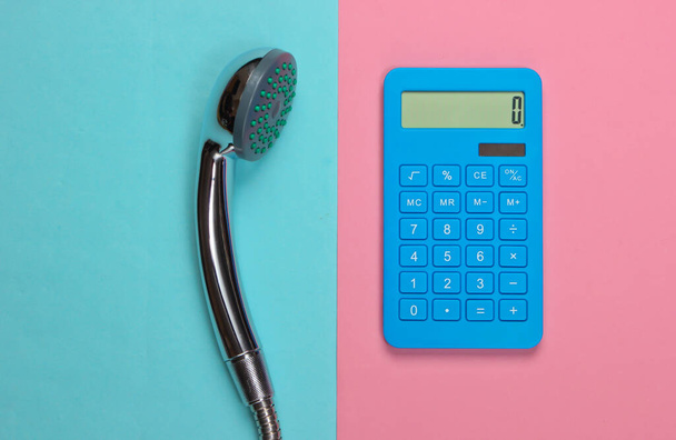 Berekening van de waterkosten. Calculator en douchekop op roze blauwe pastelachtergrond. Bovenaanzicht - Foto, afbeelding