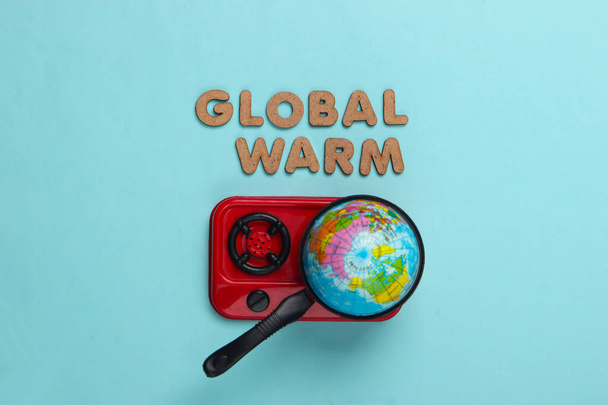 Global warming concept. Globe in pan on stove. Blue background. Top view - Fotó, kép
