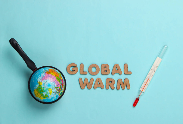 Global warming concept. Globe in pan and thermometer. Blue background. Top view - Foto, Bild