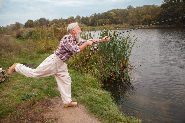 tiro de longitud completa de un hombre mayor barbudo divertirse, la pesca en un lago - Foto, Imagen