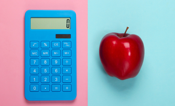 Kalkulator i czerwone jabłko na niebiesko-różowym pastelowym tle. Koncepcja edukacji. Widok z góry - Zdjęcie, obraz