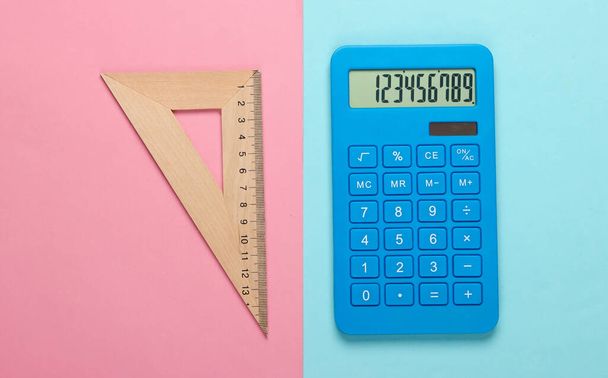 Kalkulator i drewniany linijka trójkąt na niebiesko-różowy pastelowy tło. Koncepcja edukacji. Widok z góry - Zdjęcie, obraz