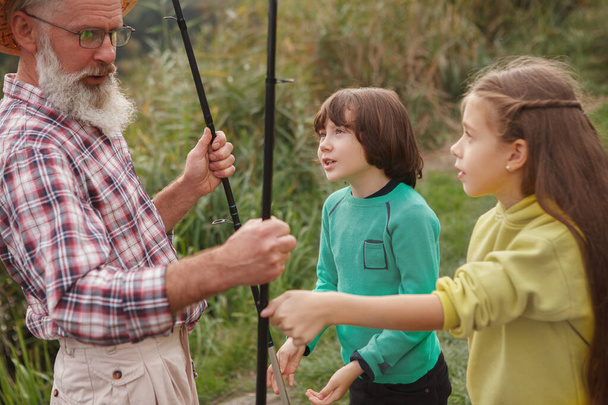 Двое очаровательных детей узнают о рыбалке от своего дедушки-рыбака - Фото, изображение