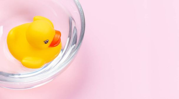 One rubber duck floating in the water in glass bowl, pink background with place for copy space, horizontal, top view - Foto, Imagem