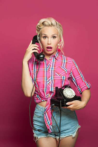 Surprised shocked pin-up woman answers a phone call on pink - Fotó, kép