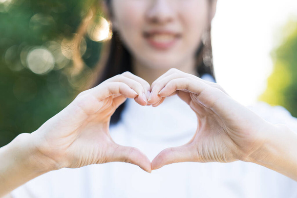 Женщина в белом халате, создающая форму сердца обеими руками. - Фото, изображение