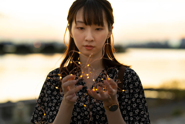 aziatische jong vrouw wikkeling een verlichting licht met beide handen - Foto, afbeelding