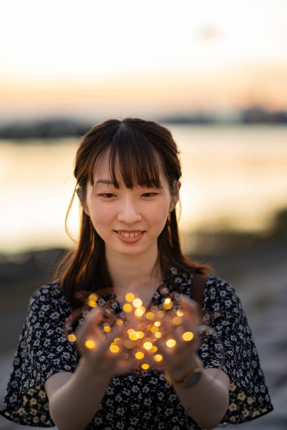 Mujer joven asiática envolviendo una luz de iluminación con ambas manos - Foto, Imagen