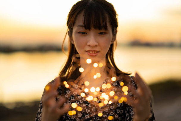 Asyalı genç bir kadın iki eliyle aydınlatma ışığını sarıyor. - Fotoğraf, Görsel