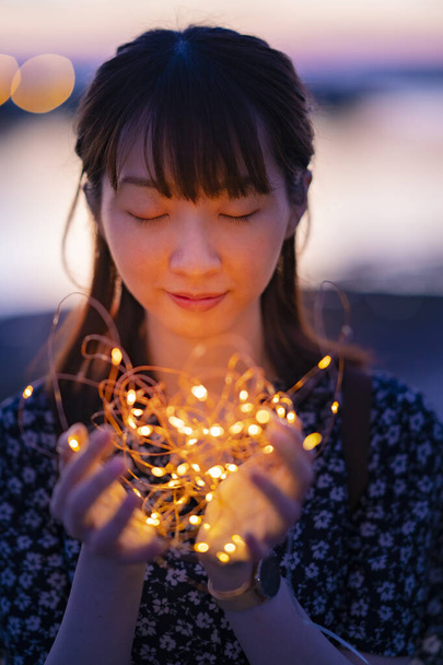 Asiatique jeune femme enveloppant une lumière d'illumination avec les deux mains - Photo, image