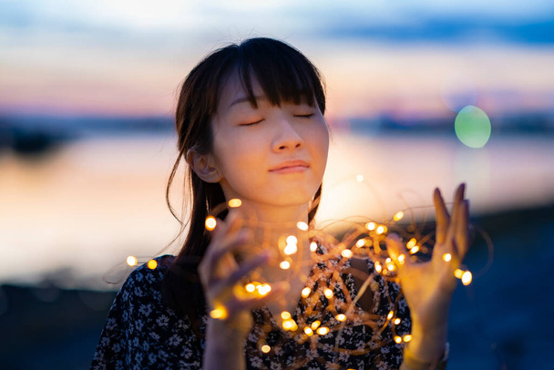 Mujer joven asiática envolviendo una luz de iluminación con ambas manos - Foto, imagen