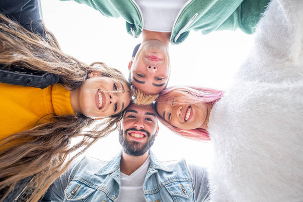 Group of four teenagers looking down arm in arm - Multicultural group of young people having fun - Friends on summer vacation looking at camera and laughing hugging each other - Foto, Imagen