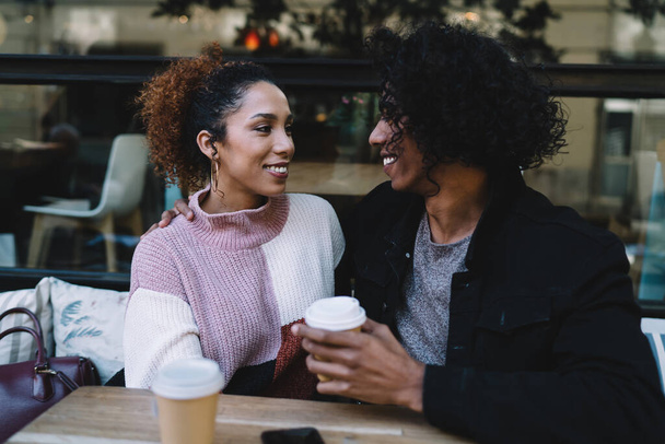 Happy multiracial young male and female looking at each other with love while sitting and drinking coffee in outdoor cafe - Fotoğraf, Görsel