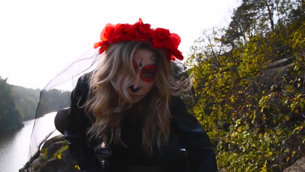 ハロウィンの映像。美しいハロウィーンの化粧スタイル。ブロンドモデルは、赤い花とシュガースカルメイクを着用。サンタ・ムエルテのコンセプト - 映像、動画
