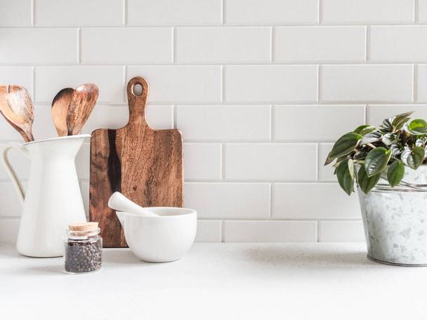 Elegante sfondo bianco cucina con utensili da cucina e pianta d'appartamento verde in piedi su piano di lavoro bianco, spazio vuoto per il testo, vista frontale - Foto, immagini
