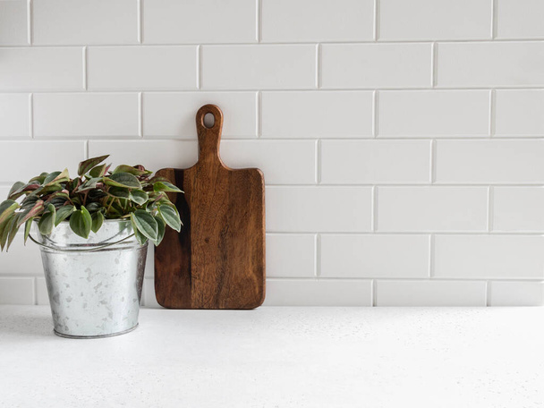 Stilvoller weißer Küchenhintergrund mit Holzschneidebrett und grüner Zimmerpflanze auf weißer Arbeitsplatte, Kopierraum für Text, Vorderansicht - Foto, Bild