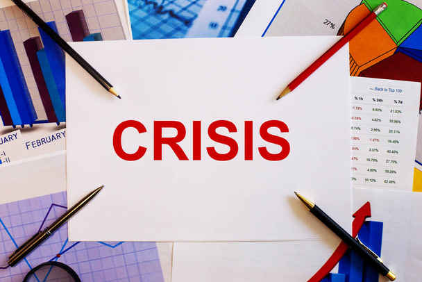 The word CRISIS is written on a white background near colored graphs, pens and pencils. Business concept - Fotó, kép