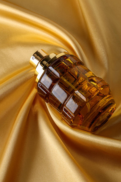 Perfume bottle on Gold silk folded fabric background fragrance perfume bottle on dark empty background. Top view.  - Photo, image