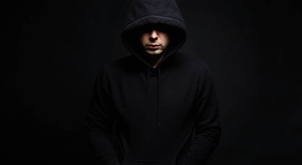 Mann mit schwarzer Kapuze posiert im dunklen Studio. Junge im Kapuzenpulli. Männerporträt - Foto, Bild