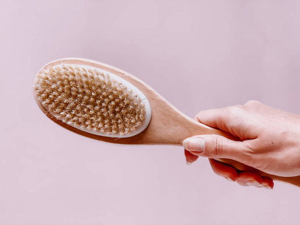 Brush with a handle for dry anti-cellulite massage or brushing in the hand of a girl in soft pink colors.  Beauty concept. - Foto, Imagem