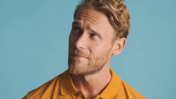 Attractive blond bearded man looking thoughtful posing on camera isolated on blue background - Foto, Imagem