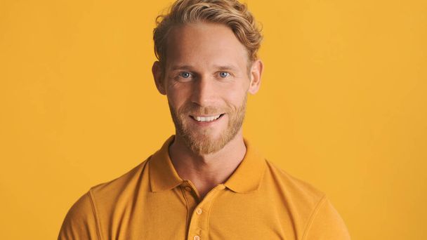 bel homme barbu blond positif regardant joyeusement dans la caméra et souriant isolé sur fond jaune - Photo, image