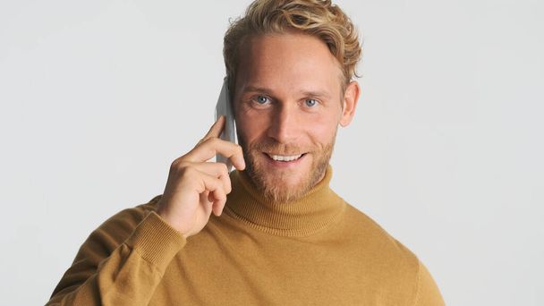 Jóképű mosolygós szőke szakállas férfi beszél okostelefon néz magabiztos a kamera felett fehér háttér - Fotó, kép