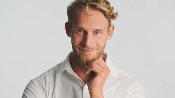 Atraente sorrindo loiro barbudo homem confiantemente olhando para a câmera e sorrindo sobre fundo branco - Foto, Imagem
