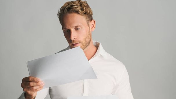 Jovem loiro concentrado barbudo empresário em camisa trabalhando com documentos de negócios isolados em fundo branco - Foto, Imagem