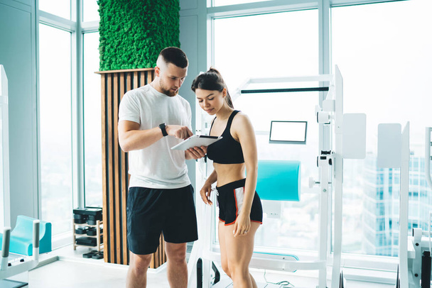 Determined young sportspeople in sportswear chilling in modern spacious light gym and talking to each other while choosing sport exercises - Foto, Imagen