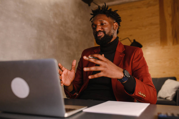 Confident young african man look at webcam conference video calling in office, happy mixed race entrepreneur talking doing online video chat job interview sit at desk - Foto, Imagen
