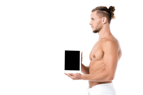 boční pohled na sexy muže bez trička v ručníku prezentující digitální tablet izolované na bílém - Fotografie, Obrázek