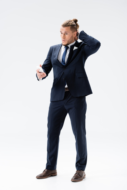confused young businessman in suit with smartphone isolated on white - Foto, Imagem