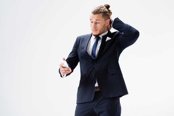 confused young businessman in suit with smartphone isolated on white - Φωτογραφία, εικόνα