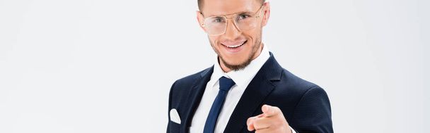 feliz joven hombre de negocios en traje y gafas apuntando a la cámara aislada en blanco, pancarta - Foto, Imagen