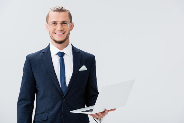 usmívající se mladý podnikatel v obleku a brýle s notebookem izolované na bílém - Fotografie, Obrázek