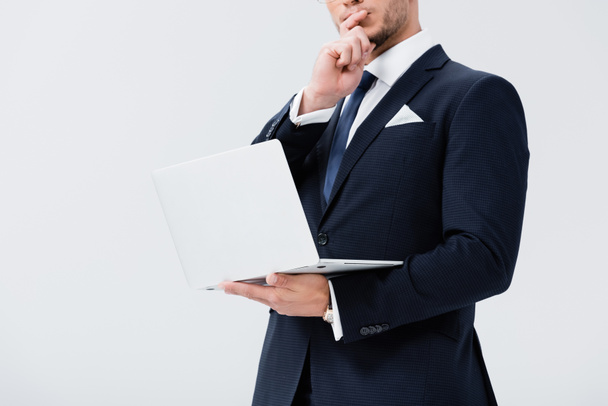 bijgesneden weergave van pensive jonge zakenman in pak met laptop geïsoleerd op wit - Foto, afbeelding