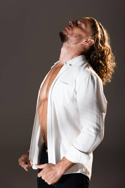 sexy man with unbuttoned shirt posing on dark background - Фото, зображення
