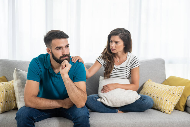 Young couple woman and man sitting on the sofa in the living room had an argue and not talking where girlfriend put her hand on the boyfriend shoulder and try to calm him down, relationship issues - 写真・画像