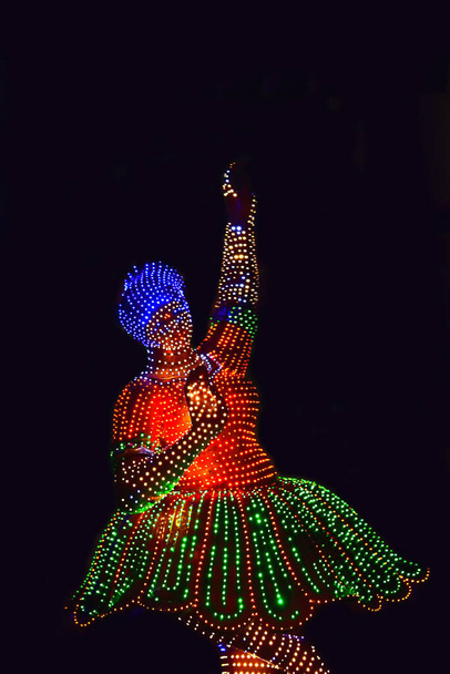 Merry-go-round μοντέλο στο σκοτάδι, φωτίζεται από πολλούς πολύχρωμους λαμπτήρες LED τυλιγμένο γύρω από τη δομή του. - Φωτογραφία, εικόνα
