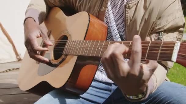 Closeup de irreconhecível afro-americano homem dedos tocando cordas de guitarra de madeira tocando melodia sentado fora desfrutando de verão - Filmagem, Vídeo
