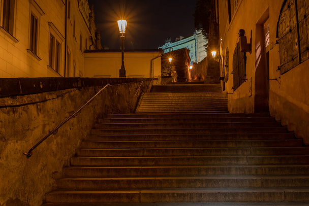 light from a lit street light in a city street at night. glowing lamp at night in the old town of prague in the czech republic - Fotó, kép