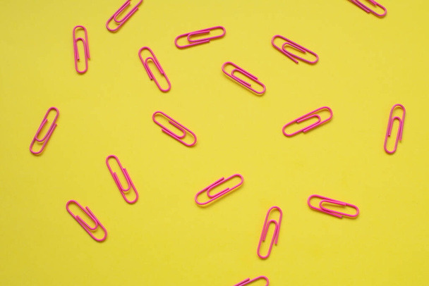 Clipes de papel rosa dispostos aleatoriamente sobre um fundo amarelo brilhante - Foto, Imagem