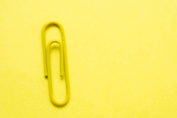 Clipe de papel amarelo sobre um fundo amarelo brilhante, com espaço de cópia no lado direito da foto - Foto, Imagem