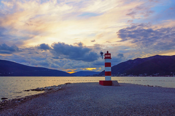 Herbstlicher Sonnenuntergang, abends mediterrane Landschaft. Rot-weiß gestreiftes Leuchtfeuer an der Küste der Bucht von Kotor in der Nähe der Stadt Tivat. Montenegro - Foto, Bild