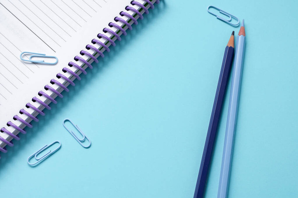kék fa színű ceruzák, gemkapcsok és egy notebook egy fényes kék háttér, némi másolási hely - Fotó, kép